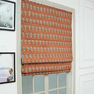 Può includere: Una tenda a pacchetto installata su una finestra, caratterizzata da una base in tessuto color arancio bruciato con un motivo ripetitivo di piccoli elementi floreali chiari disposti in colonne verticali su tutta la superficie.