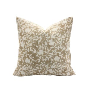 May include: A square cushion featuring a beige backdrop and a white floral design. The cushion has a soft, textured look, suitable for home decor. The floral pattern is a repeating design of stylized flowers and vines.