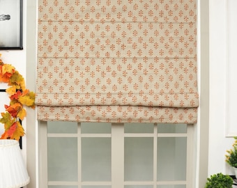 May include: A beige Roman shade window covering featuring a repeating pattern of small, rust-colored floral motifs. The fabric shade is partially raised, displaying horizontal folds across the surface, and is mounted within a light-colored window frame.