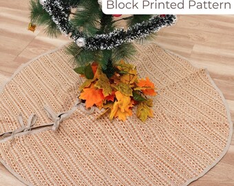May include: A beige Christmas tree skirt with a block printed pattern. The skirt has a light brown border and a tie closure. The text "Block Printed Pattern" is visible. The skirt is under a Christmas tree decorated with tinsel and ornaments.