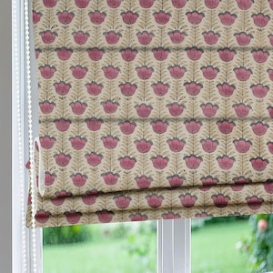 Op de afbeelding: Een Romeins rolgordijn met bloemenpatroon. Het ontwerp toont herhaalde roze bloemmotieven met grijze accenten op een beige achtergrond. Het rolgordijn is gedeeltelijk opgetrokken en toont de gelaagde plooien en een kralenkoord.