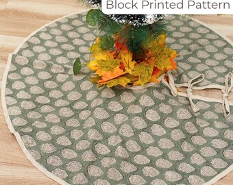 May include: A round, sage green Christmas tree skirt with a block-printed pattern of beige leaf shapes. The skirt has a cream-colored border and ties. The text "Block Printed Pattern" is visible in the image.