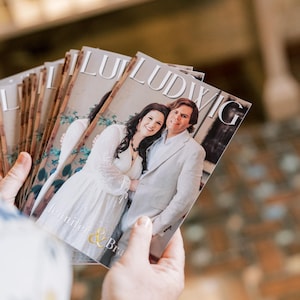 May include: A stack of rectangular printed cards featuring a photograph of a couple, with the text LUDWIG at the top and Jennifer & Brad at the bottom. The cards show a person in a white dress and a person in a light-colored blazer standing together.