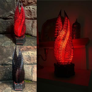 Könnte beinhalten: Eine rot-schwarze 3D-gedruckte Lampe in Form einer zweiflammigen Flamme mit einem Sockel, auf dem "MAINTENANCE" steht. Die Lampe ist eingeschaltet und strahlt ein rotes Licht ab.