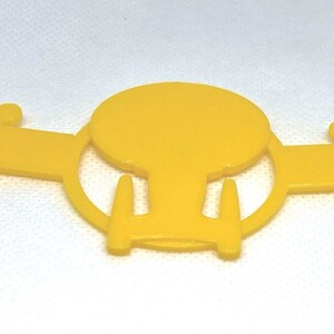 May include: Yellow plastic ear saver with a spaceship design. The ear saver has adjustable straps on both sides.
