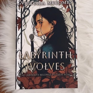 May include: A book cover featuring a woman with dark hair and a sword. The title "Labyrinth Wolves" is prominently displayed, along with the author's name, Victoria McCombs. The cover has a fantasy theme with a dark color palette.