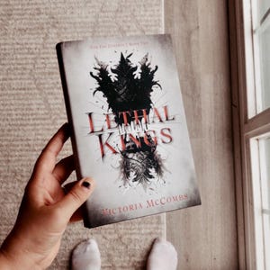 May include: A paperback book titled "Lethal Kings" by Victoria McCombs. The book cover features a black and white illustration of a creature with wings and a crown.