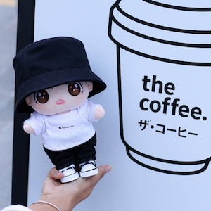 May include: A plush doll wearing a black bucket hat, white t-shirt, black pants, and sneakers. The doll is next to a sign with a coffee cup graphic and the words "the coffee." and Japanese text.
