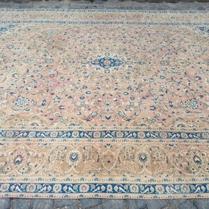 May include: A large, intricately patterned rug with a beige background and blue and green floral designs. The rug has a border with a repeating pattern of blue, white, and green.