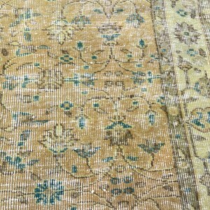 May include: Close-up of a vintage rug with a distressed, floral pattern. The rug features a warm color palette of gold, beige, and teal. The design includes stylized flowers and vines, with a faded, antique appearance.