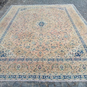 May include: A large, rectangular rug with a beige background and intricate floral patterns in shades of blue, green, and pink. The rug has a border with a repeating pattern of blue and white.
