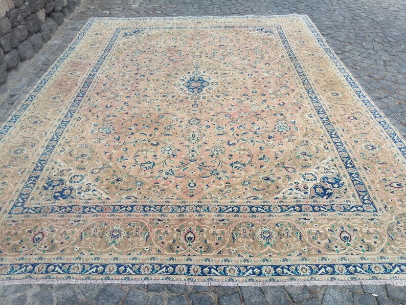 May include: A large, rectangular rug with a beige background and intricate floral patterns in shades of blue, green, and pink. The rug has a border with a repeating pattern of blue and white.