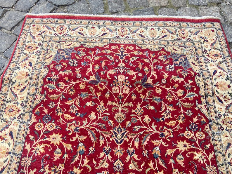 May include: A red rug with a floral pattern. The rug has a cream-colored border with a dark blue and cream-colored inner border.