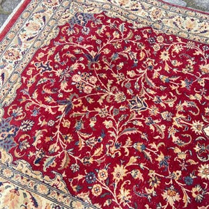 May include: A red rug with a floral pattern. The rug has a cream-colored border with a floral design.