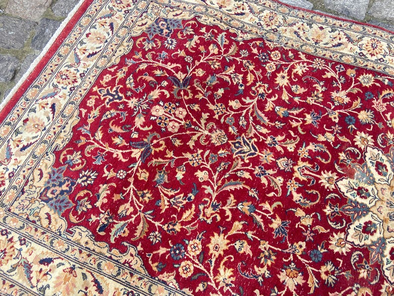 May include: A red rug with a floral pattern. The rug has a cream-colored border with a floral design.