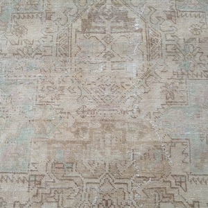May include: A vintage rug with a faded, light brown and cream color scheme. The rug has a geometric pattern with a central medallion.
