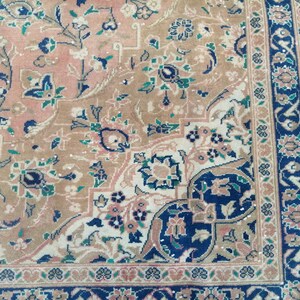 May include: A close-up of a patterned rug with a beige background and intricate floral designs in shades of blue, green, and pink. The rug has a border with a repeating pattern of blue, green, and white.