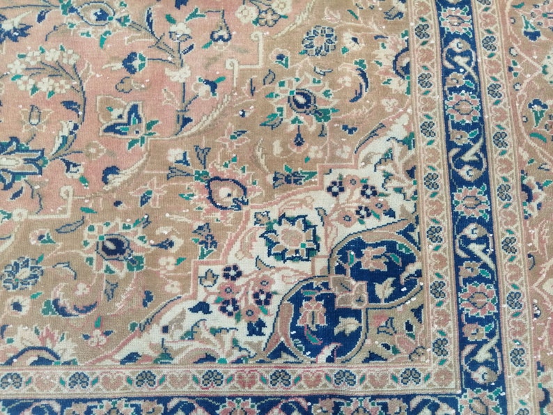 May include: A close-up of a patterned rug with a beige background and intricate floral designs in shades of blue, green, and pink. The rug has a border with a repeating pattern of blue, green, and white.