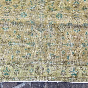 May include: A distressed, vintage-style rug with a detailed floral pattern. The rug features a color palette of muted greens, browns, and touches of turquoise. The design includes a border with stylized floral motifs, adding to its antique aesthetic.