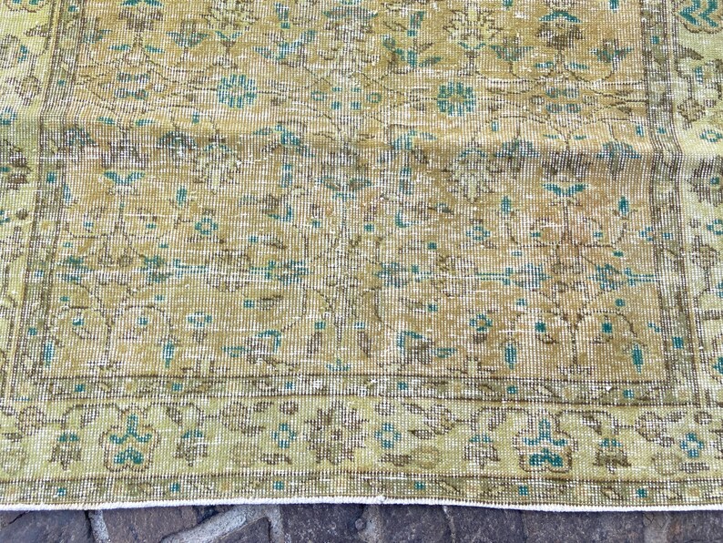 May include: A distressed, vintage-style rug with a detailed floral pattern. The rug features a color palette of muted greens, browns, and touches of turquoise. The design includes a border with stylized floral motifs, adding to its antique aesthetic.