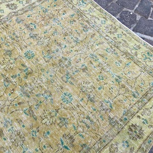 May include: An antique rug with a distressed, faded appearance. The rug features a repeating floral pattern in shades of olive green, brown, and teal. The rug's design has a vintage aesthetic, suitable for home decor.
