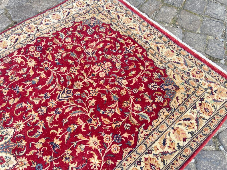 May include: A red rug with a floral pattern and a cream-colored border. The rug has a traditional design with intricate details.