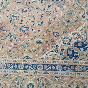 May include: A vintage rug with a floral pattern in shades of pink, blue, and beige. The rug has a detailed border with a repeating pattern.