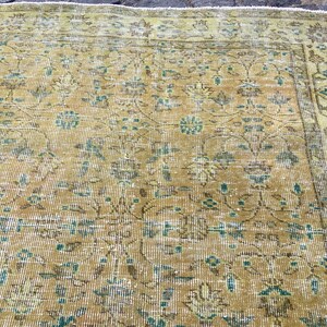 May include: A vintage rug with a distressed appearance. The rug features a central field of golden yellow with intricate floral patterns in shades of teal, brown, and cream. The border is a lighter shade of yellow. The rug has a worn, antique look.