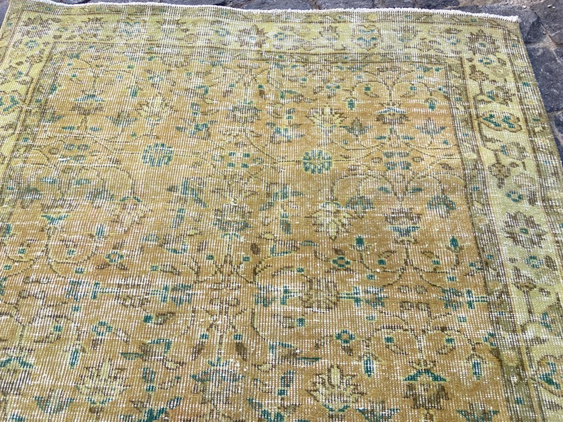 May include: A vintage rug with a distressed appearance. The rug features a central field of golden yellow with intricate floral patterns in shades of teal, brown, and cream. The border is a lighter shade of yellow. The rug has a worn, antique look.