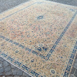 May include: A beige rug with a floral pattern and a blue border. The rug has a traditional Persian design.