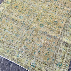 May include: A vintage-style rug with a distressed appearance. The rug features a faded color palette of yellow, green, and blue, with an intricate floral pattern. The edges are bordered with a darker shade of green, creating a classic look.