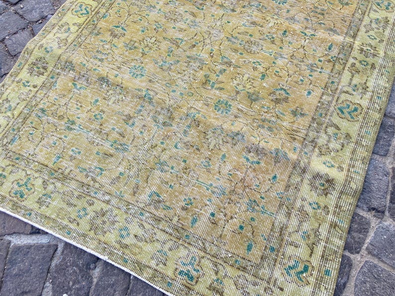 May include: A vintage-style rug with a distressed appearance. The rug features a faded color palette of yellow, green, and blue, with an intricate floral pattern. The edges are bordered with a darker shade of green, creating a classic look.