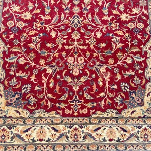 May include: A red rug with a floral pattern in cream, beige, and blue. The rug has a border with a similar floral pattern.