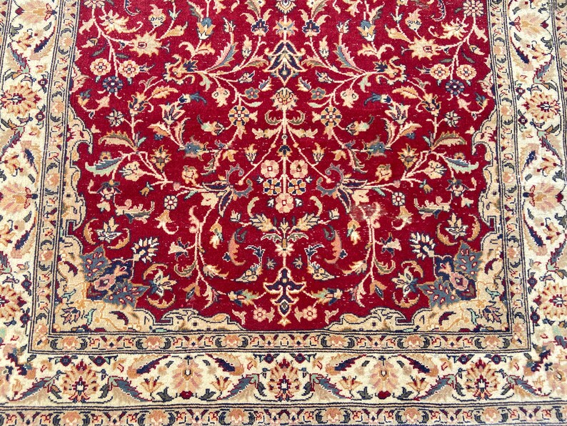 May include: A red rug with a floral pattern in cream, beige, and blue. The rug has a border with a similar floral pattern.