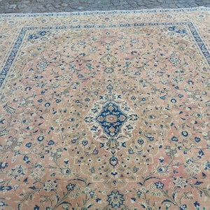 May include: A large, intricately patterned rug with a beige background and a central medallion in shades of blue, pink, and white. The rug features a floral design with delicate vines and small flowers.