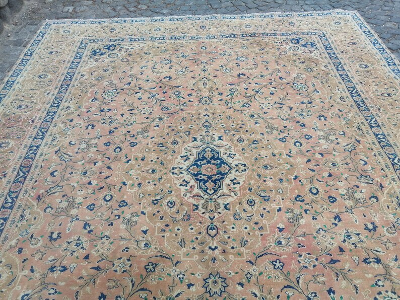 May include: A large, intricately patterned rug with a beige background and a central medallion in shades of blue, pink, and white. The rug features a floral design with delicate vines and small flowers.