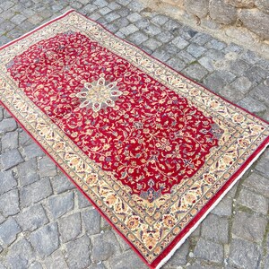 May include: A red rug with a floral pattern and a cream-colored border. The rug has a traditional Persian design.