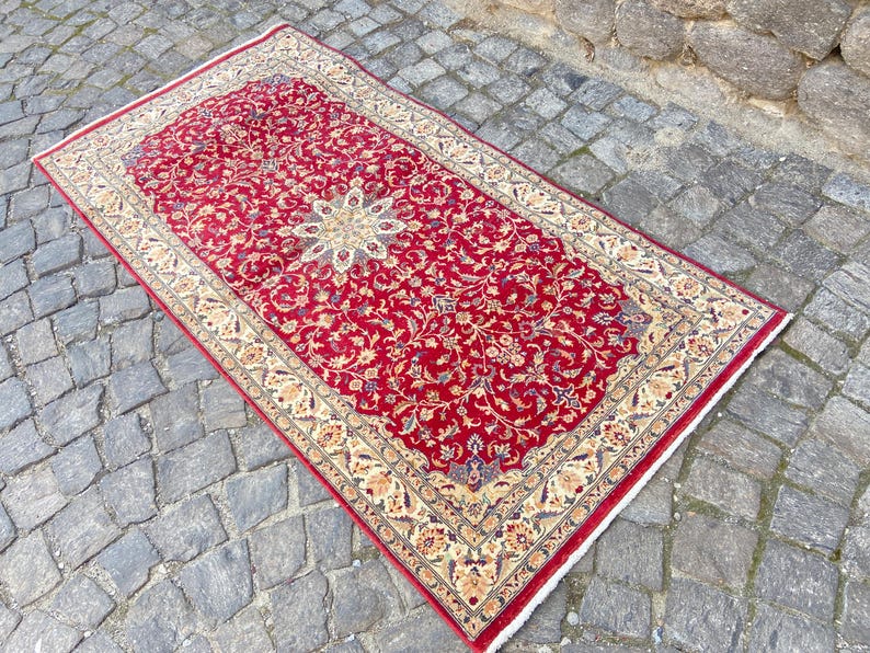 May include: A red rug with a floral pattern and a cream-colored border. The rug has a traditional Persian design.