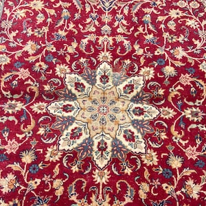 May include: A red rug with a detailed floral pattern. The center of the rug features a large, intricate starburst design with beige, blue, and cream accents.