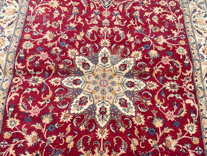 May include: A red rug with a detailed floral pattern. The center of the rug features a large, intricate starburst design with beige, blue, and cream accents.