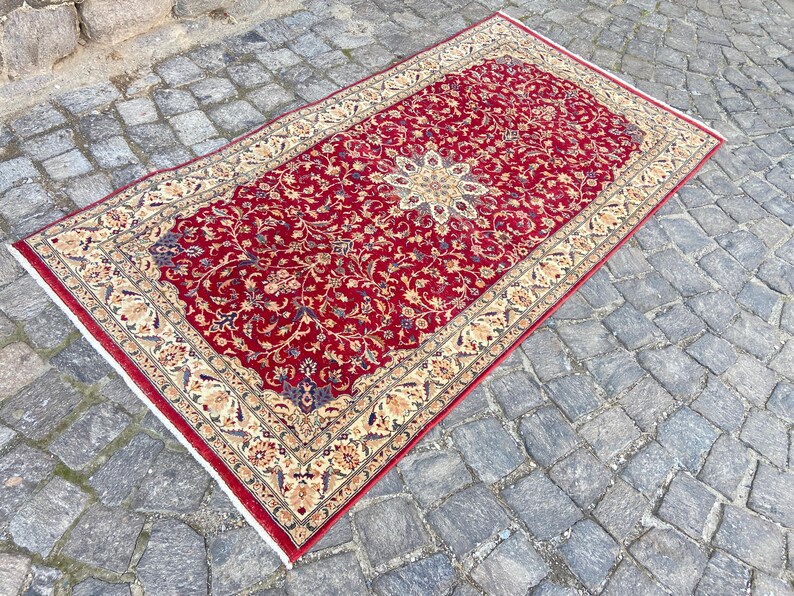 May include: A red rug with a floral pattern and a cream-colored border. The rug has a traditional design and is made of wool.