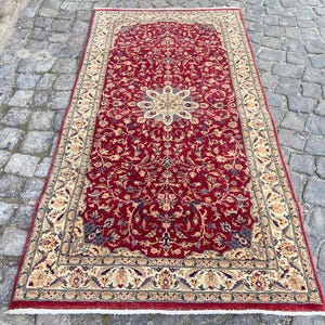 May include: A red rug with a floral pattern and a cream-colored border. The rug has a traditional Persian design.