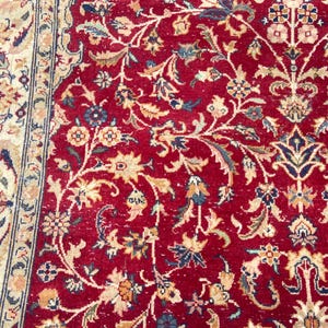 May include: A red rug with a floral pattern. The rug has a border with a cream and blue design.