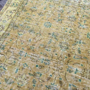 May include: Close-up of a vintage rug with a distressed, faded appearance. The rug features a warm color palette of gold, brown, and teal, with intricate floral and geometric patterns. The rug's design suggests a traditional, oriental style.