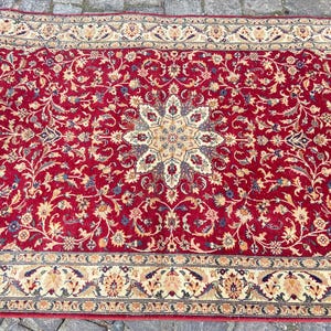 May include: A red rug with a floral pattern and a central medallion. The rug has a cream-colored border with a floral design.