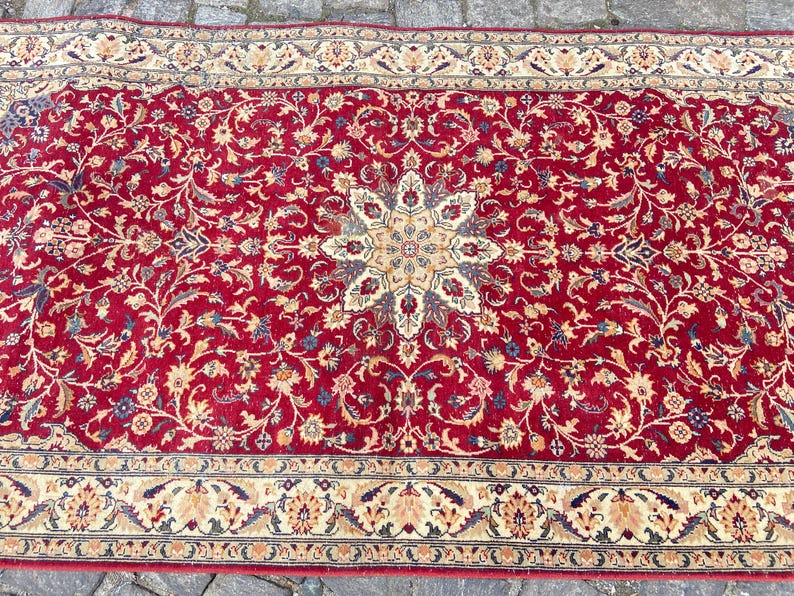 May include: A red rug with a floral pattern and a central medallion. The rug has a cream-colored border with a floral design.