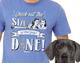 May include: A blue t-shirt with a retro-style graphic that says "Check out the size of that guy's Dane!" The graphic features a cartoon Great Dane dog and two women whispering.