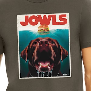 May include: A dark gray t-shirt with a vintage-style graphic of a brown labrador dog with its mouth open and drool dripping. The dog is looking up at a hamburger with the word "JOWLS" in large red letters above it.