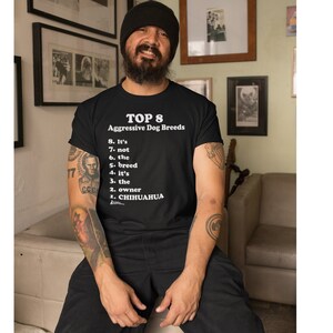 May include: A person wearing a black t-shirt with a white graphic that reads "TOP 8 Aggressive Dog Breeds" and a list of reasons why breed is not the determining factor in dog aggression. The list includes: "It's not the breed, it's the owner, Chihuahua."