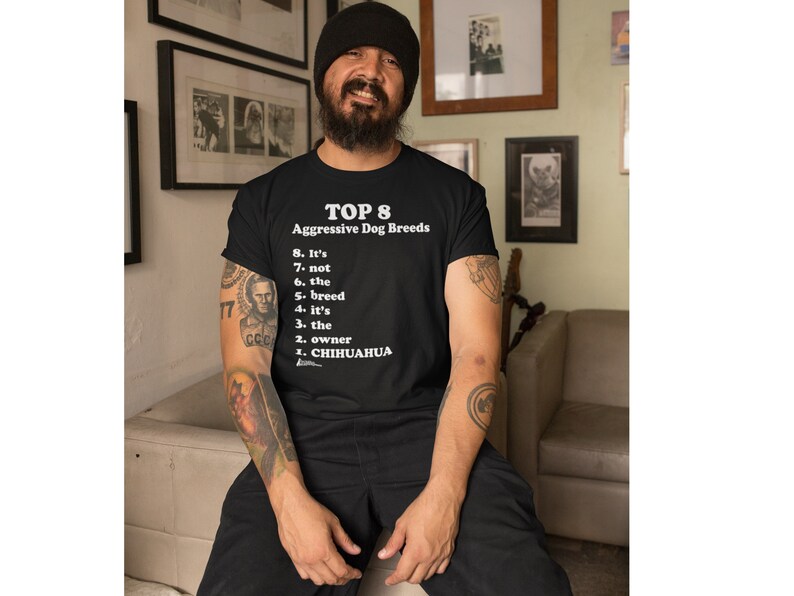 May include: A person wearing a black t-shirt with a white graphic that reads "TOP 8 Aggressive Dog Breeds" and a list of reasons why breed is not the determining factor in dog aggression. The list includes: "It's not the breed, it's the owner, Chihuahua."